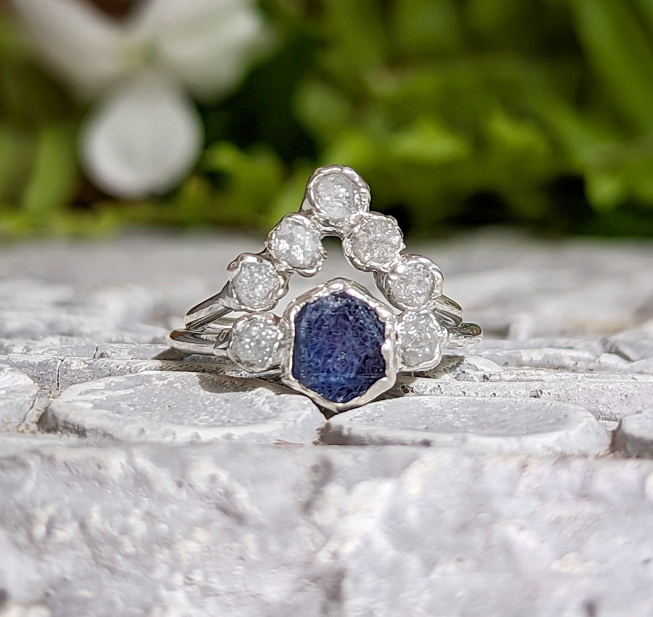 Raw sapphire and diamond wedding ring set on a stone surface, featuring a unique design in sterling silver.