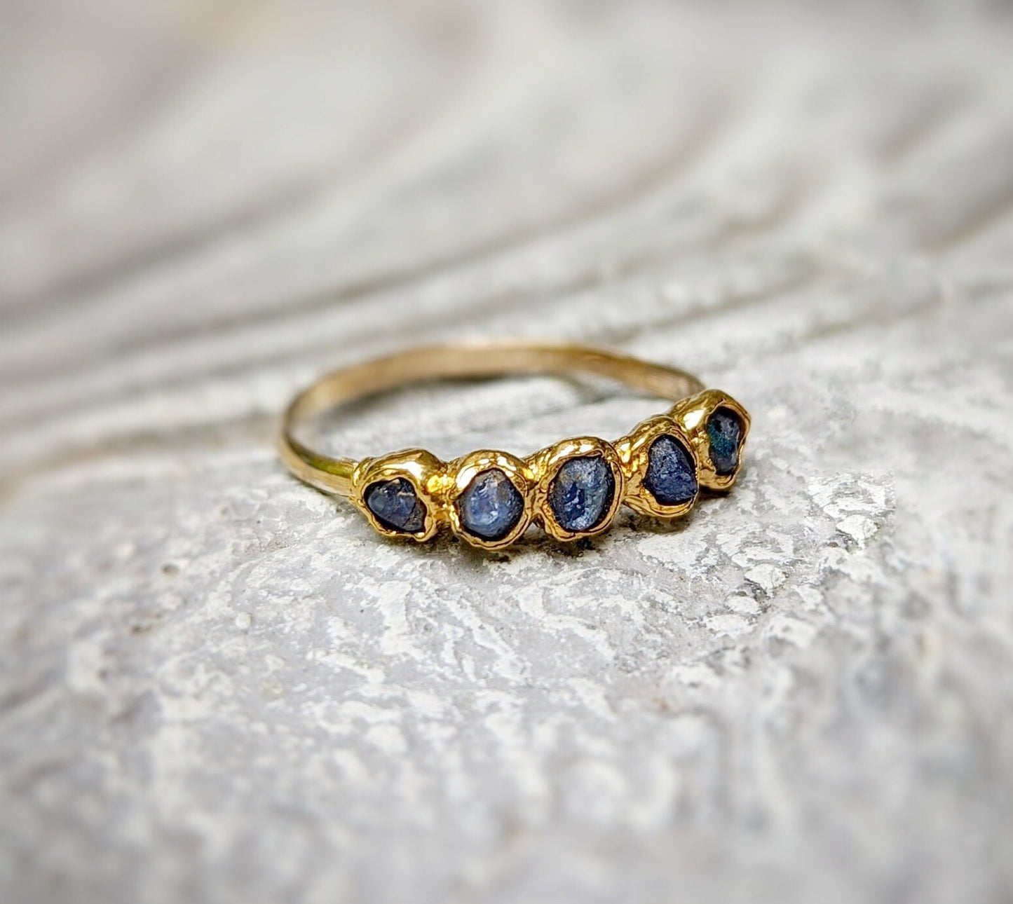 Raw sapphire multi-stone ring on a textured surface, featuring small blue sapphires set in a solid gold band.