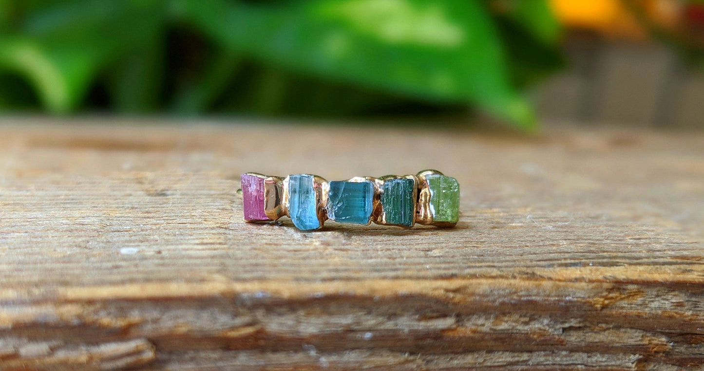 Raw Tourmaline eternity ring on a wooden surface, featuring multi-color stones set in a gold-filled band.