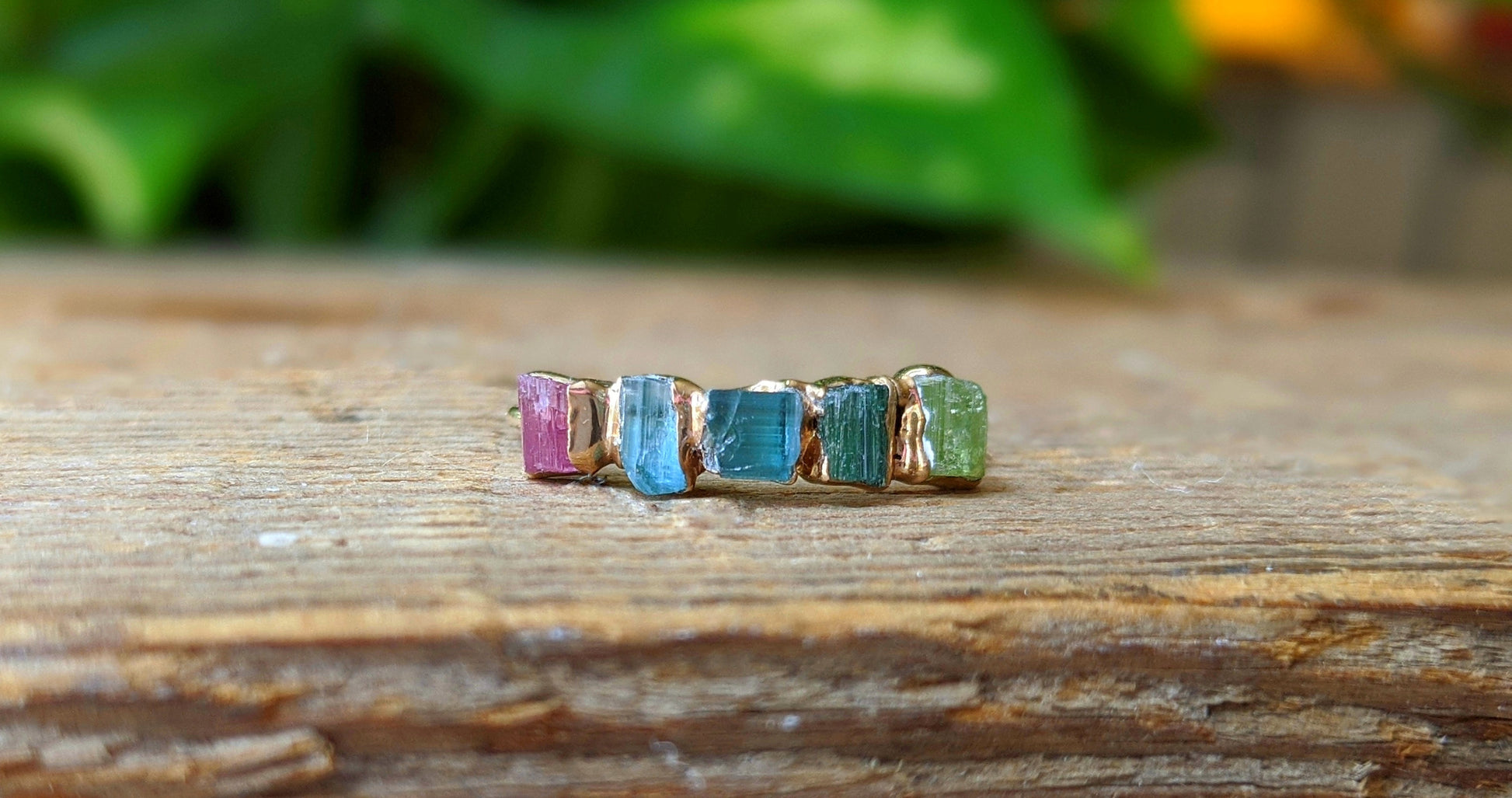 Raw Tourmaline eternity ring on a wooden surface, featuring multi-color stones set in a gold-filled band.
