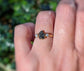 Raw uncut Black Diamond engagement ring on a finger, featuring two smaller raw diamonds, set on a 14k Gold band.