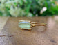 Raw yellow Apatite ring on a gold band, highlighting natural beauty, set on a wooden surface with greenery in background.