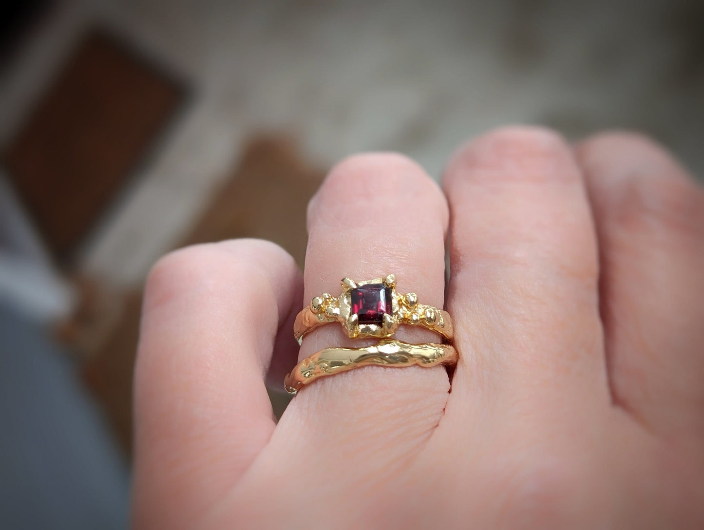 Hand wearing a handcrafted Red Garnet engagement ring set in solid 14k gold with organic textured bands.