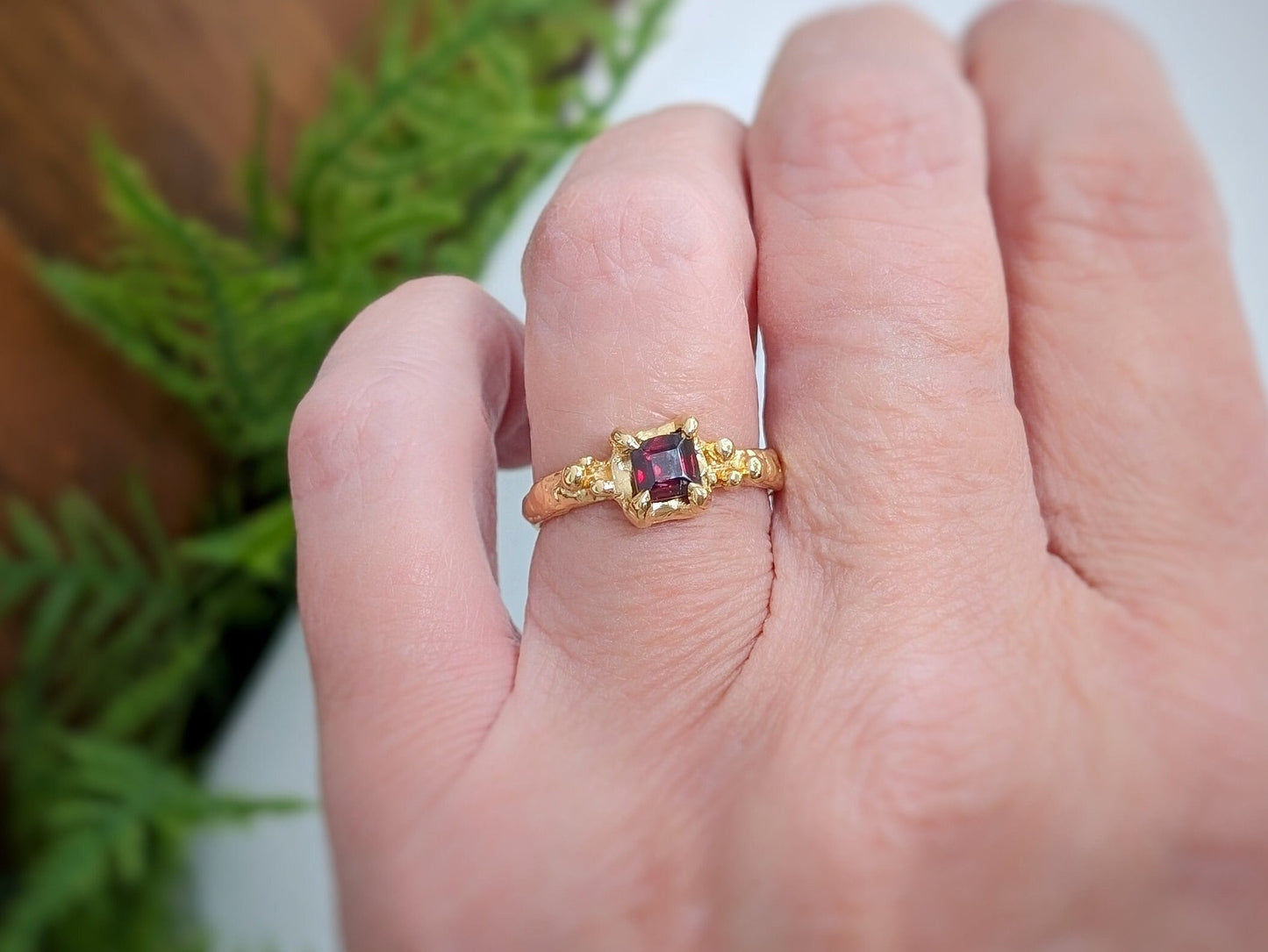 Handcrafted solid 14k gold engagement ring featuring a square red garnet crystal on a textured band.