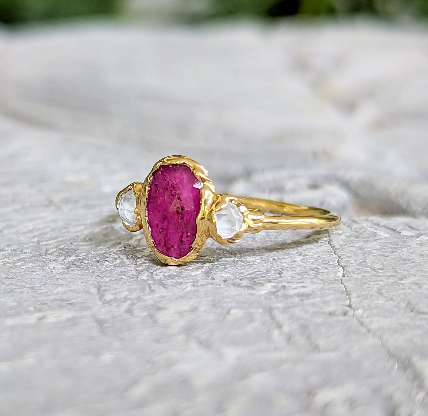 Rubellite Tourmaline and diamond engagement ring on a stone surface, showcasing its handcrafted 14k gold design.