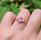 Rubellite Tourmaline and diamond engagement ring on hand, set in 14k gold, surrounded by greenery.