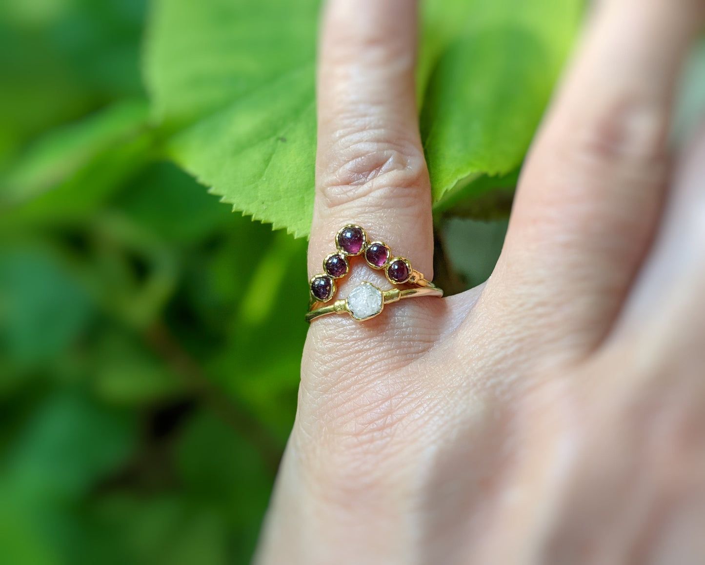 Handcrafted ruby chevron ring in 18k gold displayed on a hand surrounded by lush greenery.