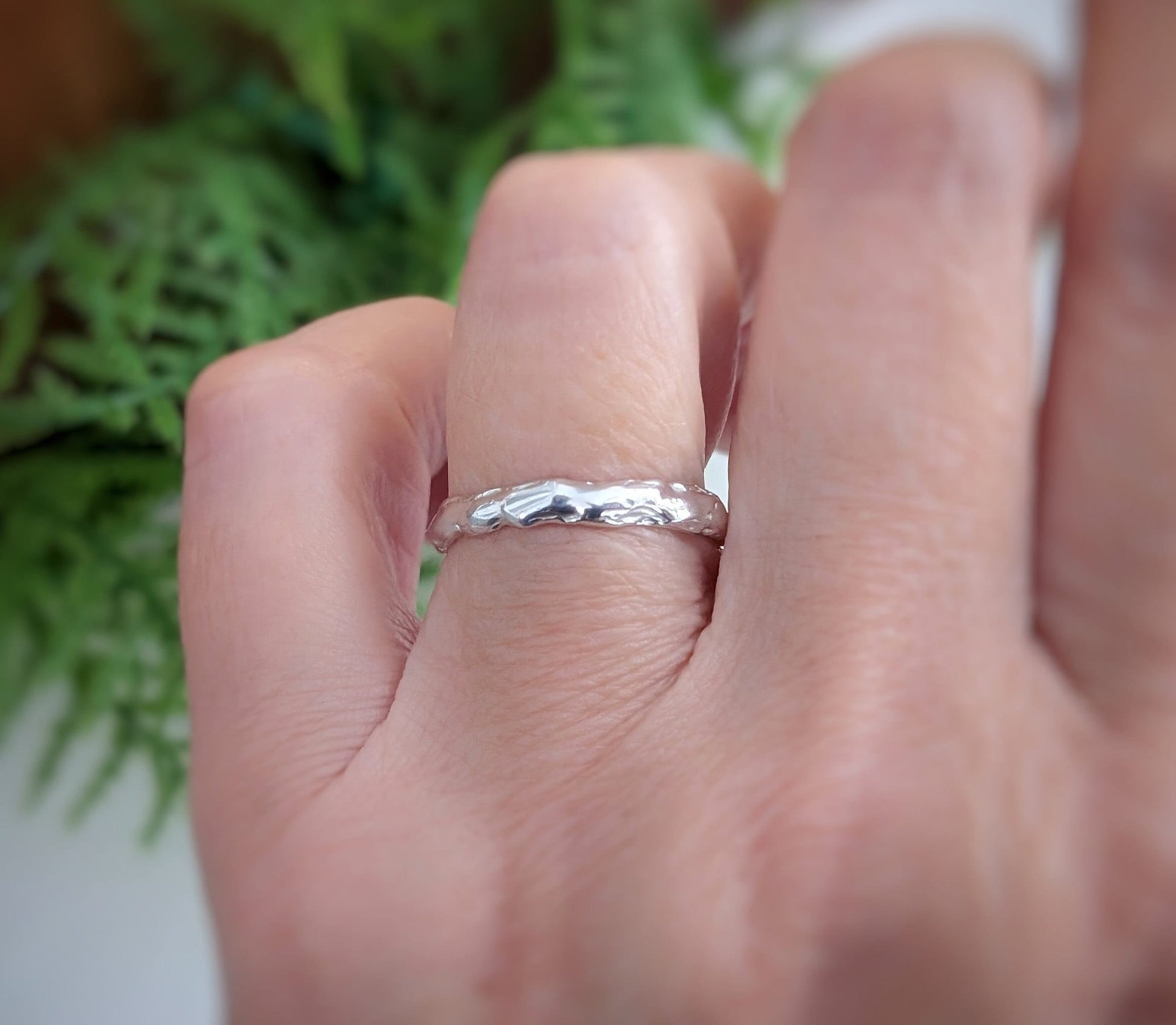 Close-up of a hand wearing a handcrafted Molten Silver wedding band, showcasing its unique abstract design.