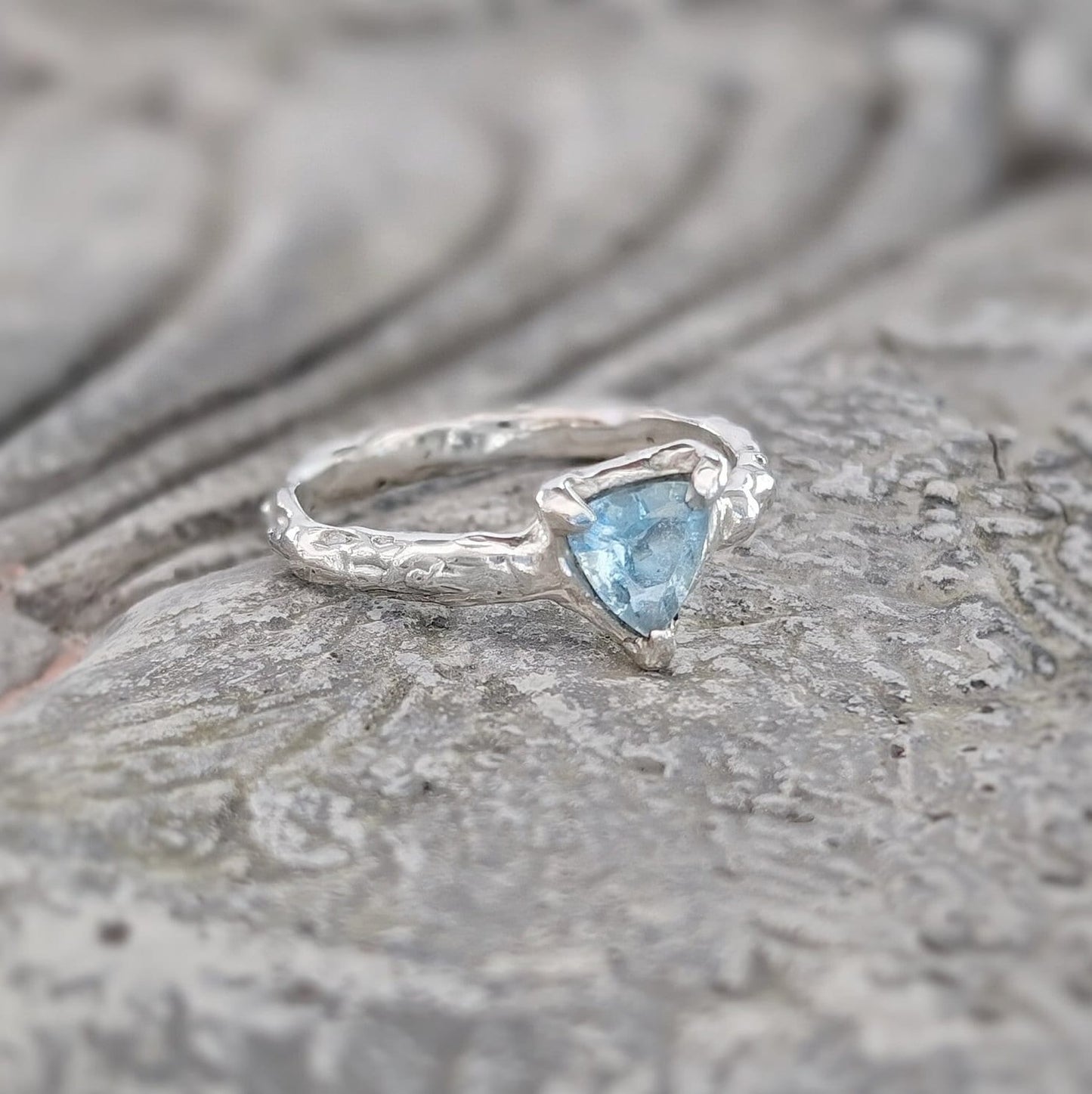 Solid Silver Aquamarine ring with trilliant cut, featuring an organic textured band, symbolizing love and individuality.