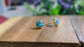 Turquoise stud earrings featuring 10mm round stones set in gold-filled posts on a wooden surface with greenery.