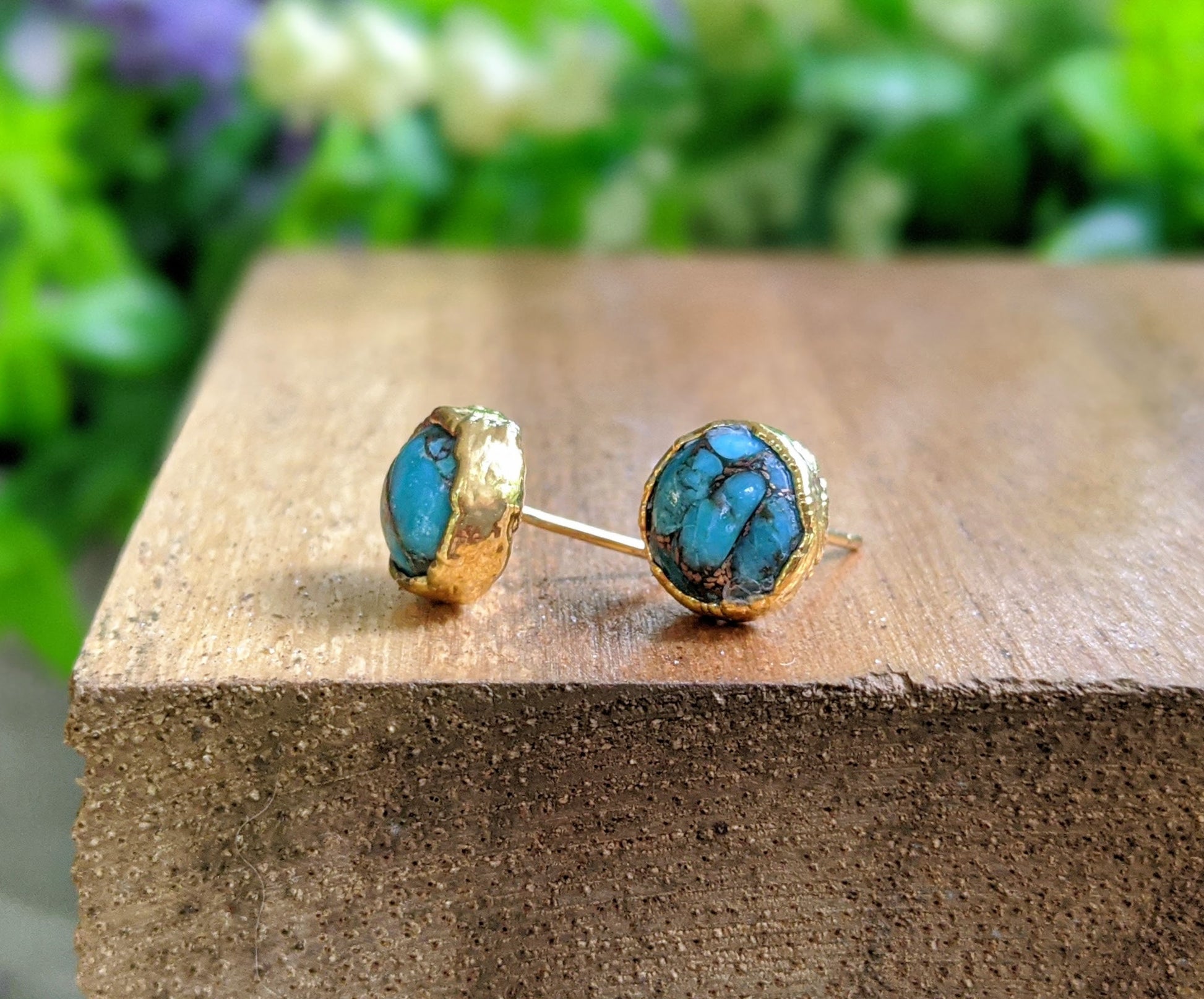 Turquoise stud earrings with gold electroformed settings on a wooden surface, showcasing classic design and unique stones.