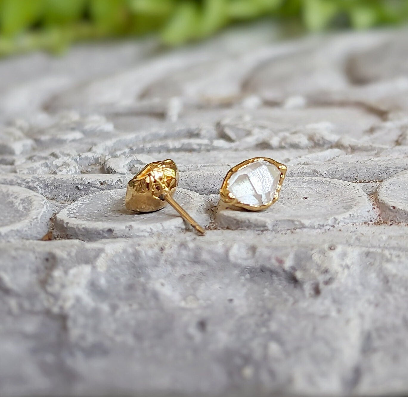 Herkimer diamond stud earrings with gold settings, showcasing raw crystal elegance on a textured stone surface.