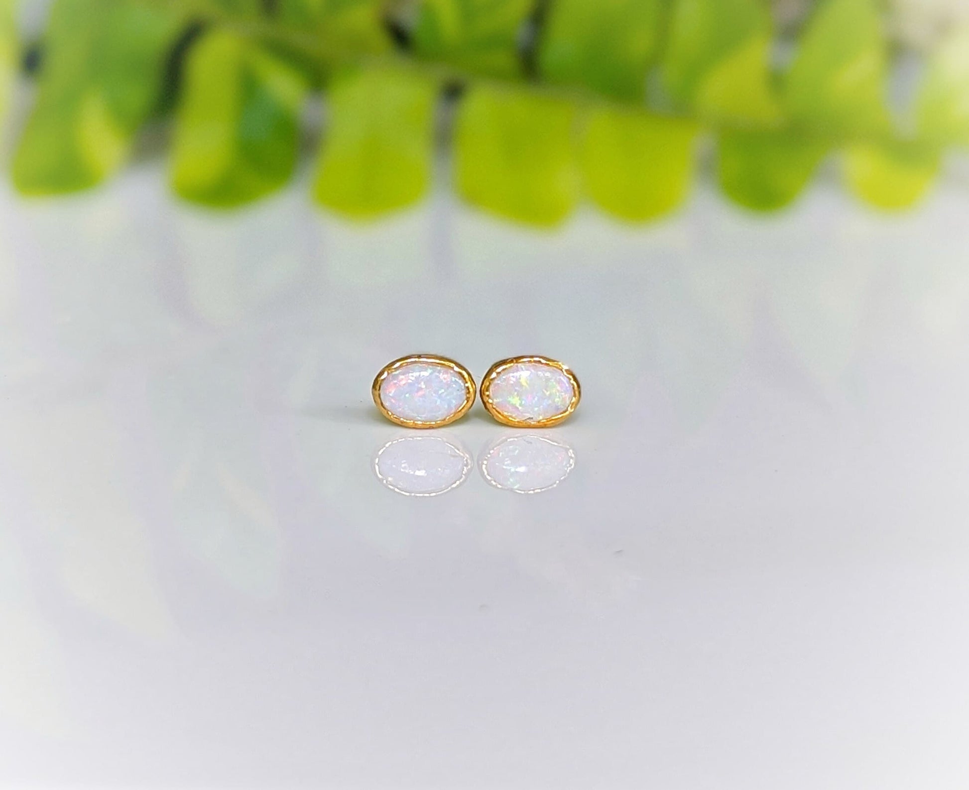 Elegant white Australian Opal stud earrings on 14k gold filled posts, reflecting light against a soft green background.